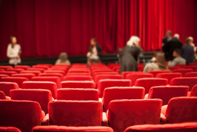 Sala teatralna z czerwonymi fotelami i czerwoną kurtyną. 