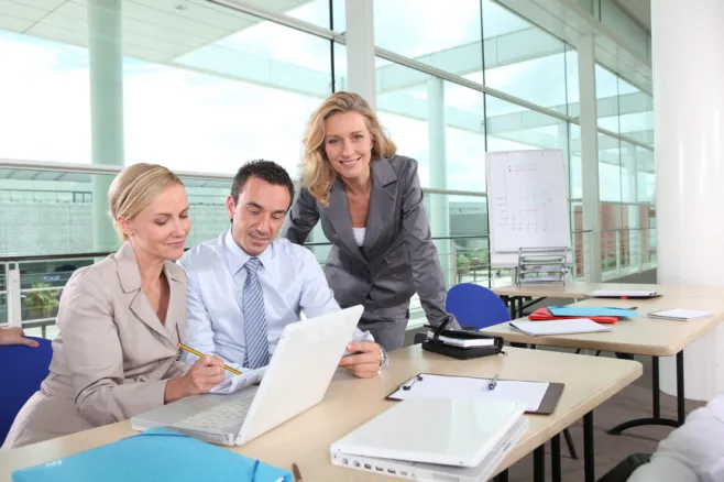 Dwie kobiety i mężczyzna patrzący na ekran laptopa w biurze