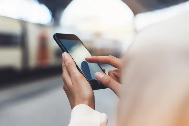 Telefon trzymany w dłoniach, w tle pociąg