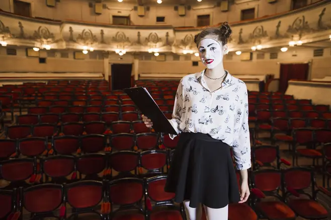 A girl wearing bold, theatrical makeup against the backdrop of a theater audience