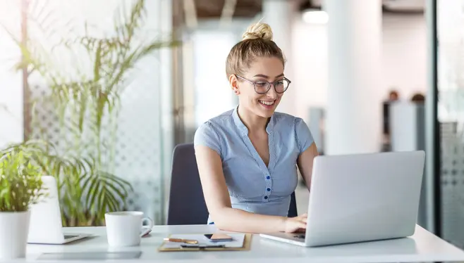 Uśmiechnięta kobieta w okularach pracuje na laptopie