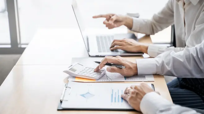 Two people discussing data on a laptop and on sheets of paper