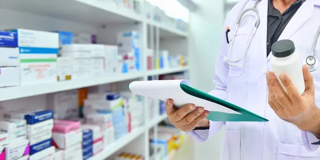 A pharmacist examining a medicine pack by a pharmacy shelf