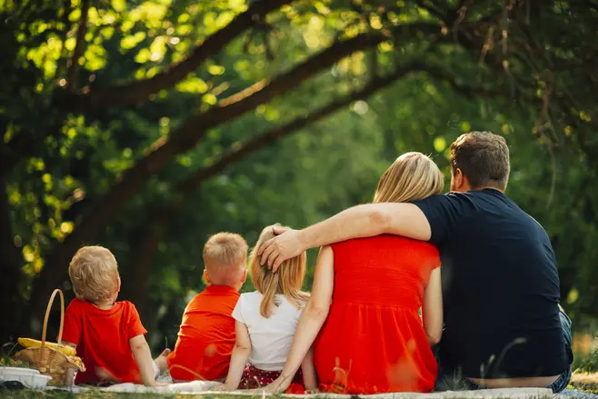 Pięcioosobowa rodzina na pikniku w lesie, na kocu siedzą rodzice i troje dzieci