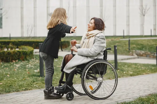 Stojąca kobieta wskazuje coś ręką przed kobietą siedzącą na wózku inwalidzkim