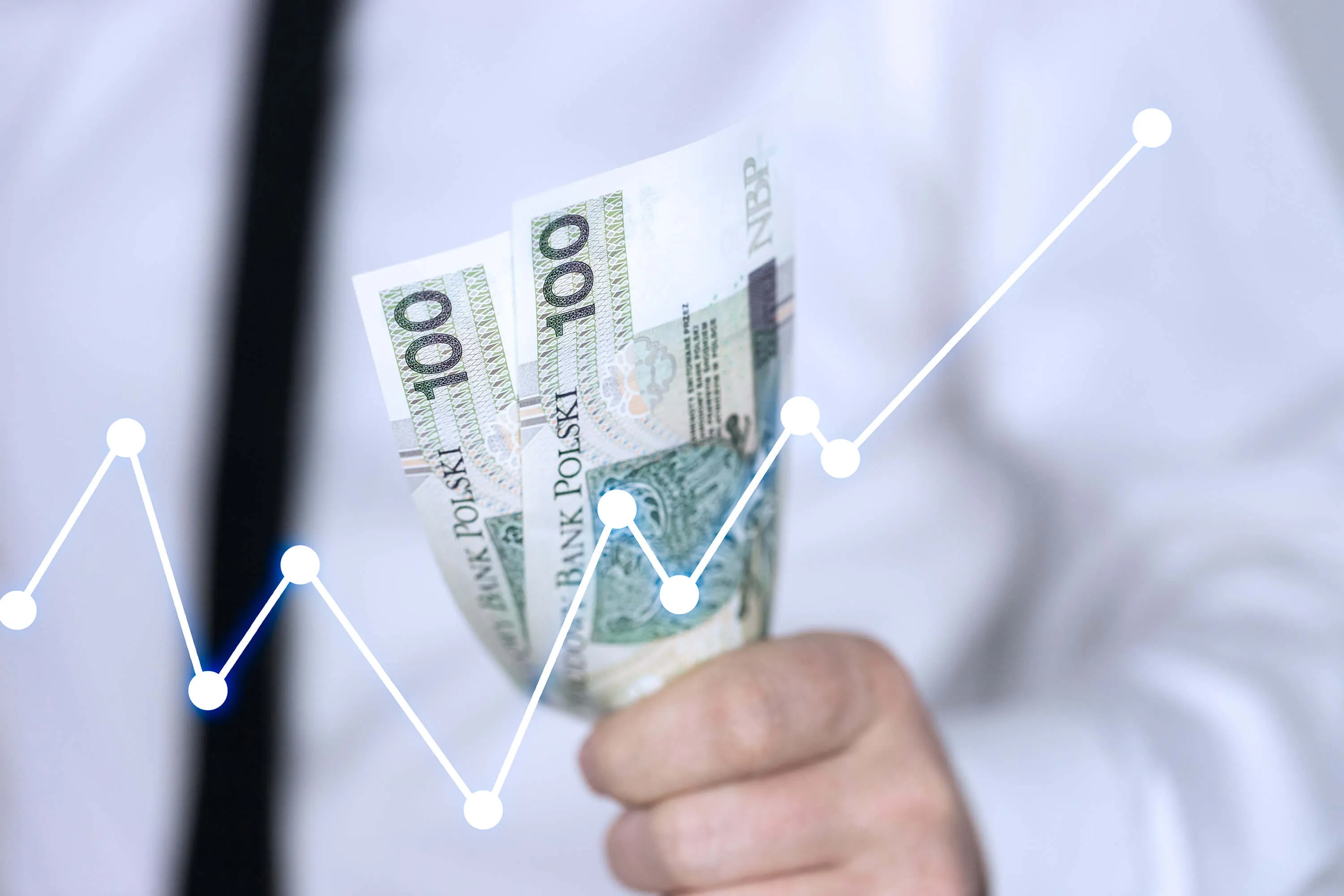 Biały wykres na tle ręki człowieka trzymającej dwa banknoty stuzłotowe.