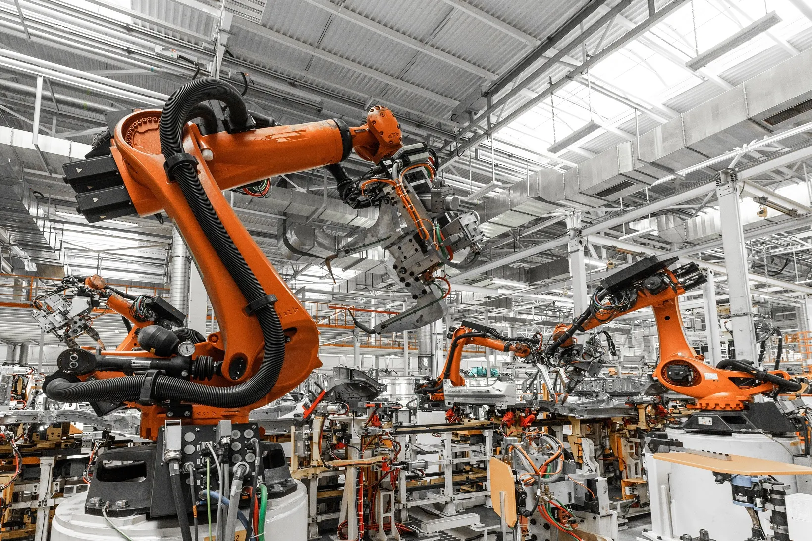 Na zdjęciu widać fabrykę z robotami, które wykonują pracę. 