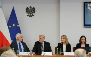 Powiększ obraz: 4 osoby za stołem prezydialnym